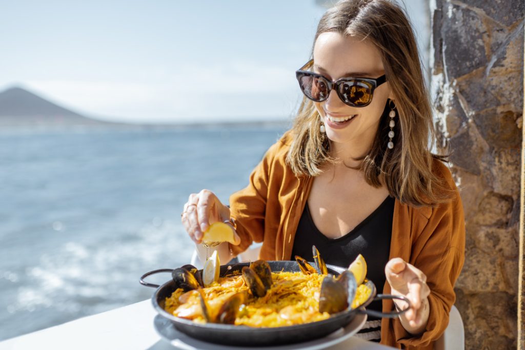 Conoce el mejor sabor de la Costa Blanca, mujer comiendo una paella con vistas al Mediterráneo